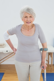 Portrait of a senior woman with crutch standing in the hospital gym